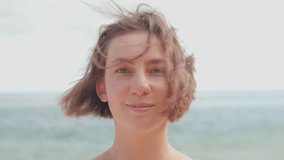 Young woman smiling at camera with wind blowing through her hair enjoying fresh air against sea representing positive energy, happiness and confidence. Closeup portrait - Powered by Shutterstock - Get 15% off with code: PIKWIZARD15
