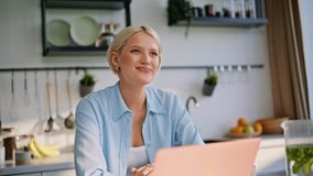 Dreamy lady thinking ideas working laptop at kitchen closeup. Smiling blonde woman in blue shirt drinking tea sitting apartment desk. Calm businesswoman looking computer screen developing project - Powered by Shutterstock - Get 15% off with code: PIKWIZARD15
