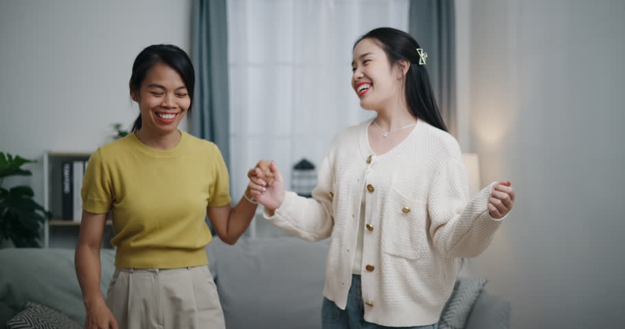 Handheld front view shot, Asian LGBTQ couple dancing together carefree in a room full of love and warmth at home. Couple spending time together.