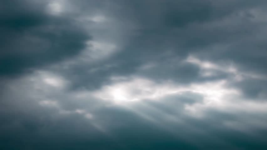 Dramatic sky with dark storm clouds and sun rays shining through the openings