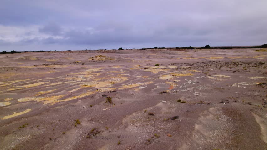 Semi orbit shot of a barren petrified ocean floor with layered textures and mineral formations under cloudy sky.