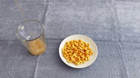 A glass of frothy drink placed next to a white bowl filled with golden roasted peanuts on a soft gray surface, creating a simple and cozy snack setup for casual enjoyment - Powered by Shutterstock - Get 15% off with code: PIKWIZARD15