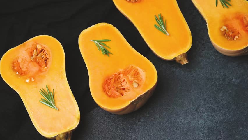 Halved butternut squash with rosemary sprigs on a dark textured background.