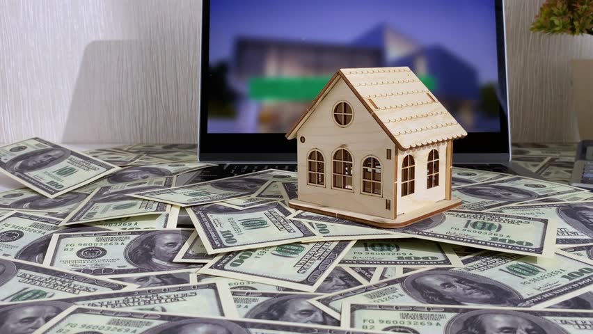 Real estate house model next to laptop and many dollars US. Real estate investment, mortgage, real estate concept.