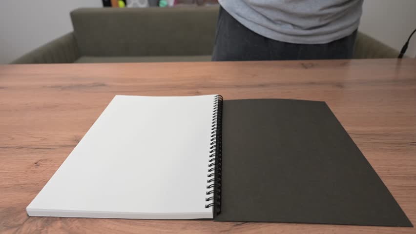 Close up revealing hands methodically turning pages of spiral notebook resting on wooden surface, showcasing blank writing space for creative documentation