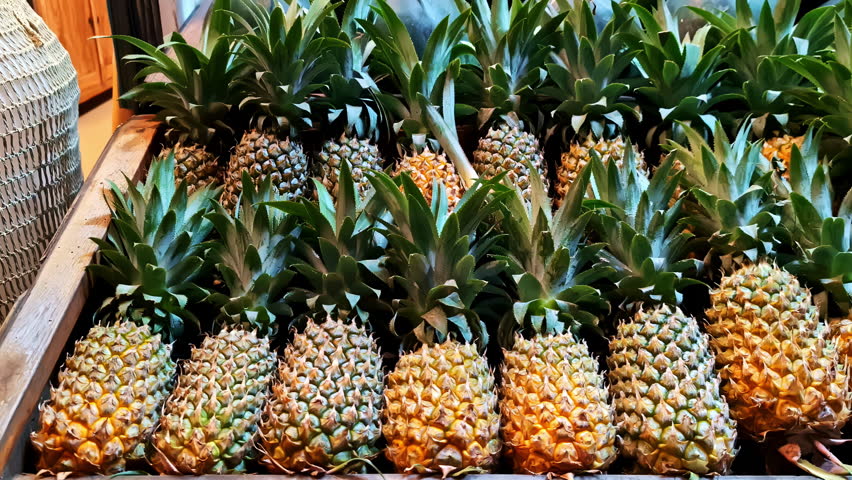 Ripe pineapples line the display case of a fresh fruit and vegetable shop.