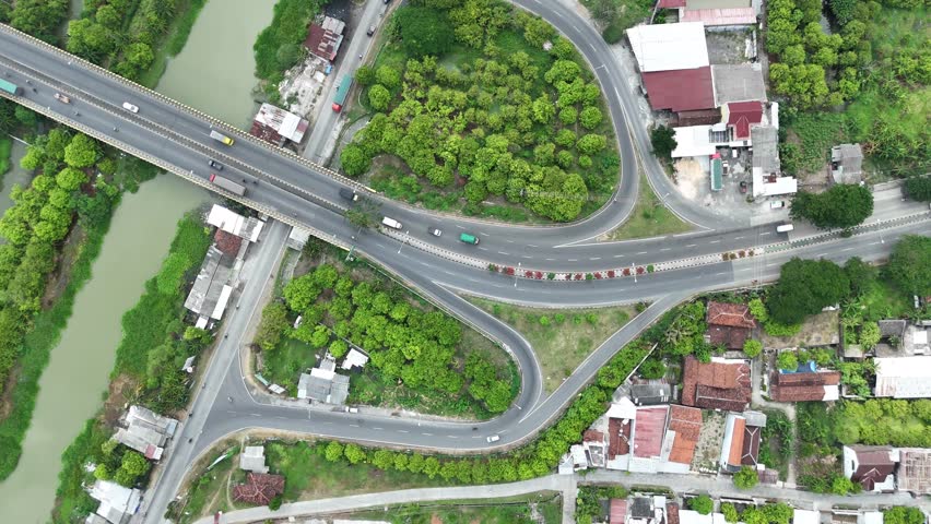 Aerial view of a bridge with dense trees and road curves on a river with vehicles