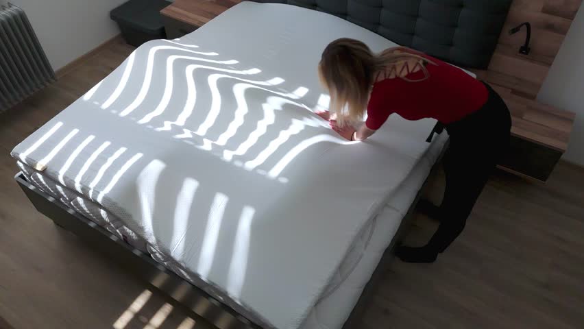 Woman placing and adjusting a mattress topper on a modern bed. Concept of home comfort, bedroom interior, healthy sleep, and lifestyle care for better rest and relaxation