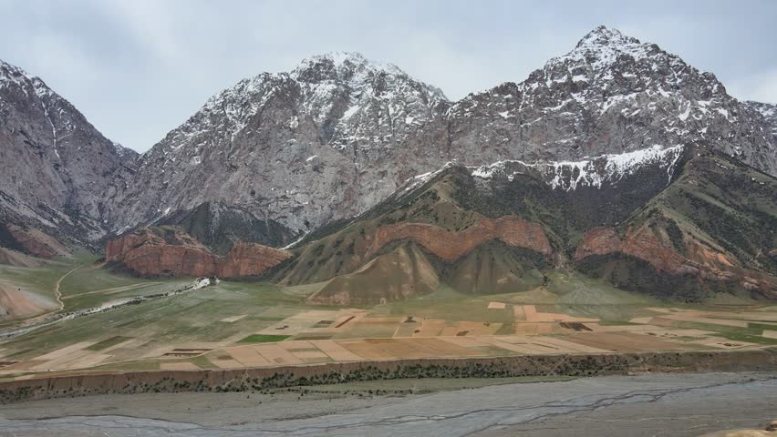 Drone clip of the Pamir Highway running through mountainous terrain. Snow-covered peaks rise in the background, while dry, snowless fields stretch along the roadside.	