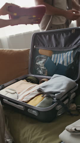 Vertical shot of unrecognizable couple working in team while packing their suitcase with perfectly folded clothes, getting ready for romantic trip, journey or vacation