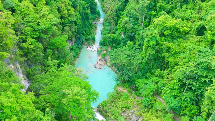 Aerial view of Kuang Si Falls, with turquoise multi-tiered pools, green jungle, and people swimming in the water in Laos.