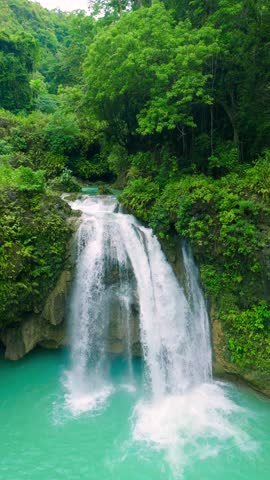 Aerial view of the multi-tiered Kuang Si Falls featuring vibrant turquoise water cascading through lush green jungle foliage, Laos.