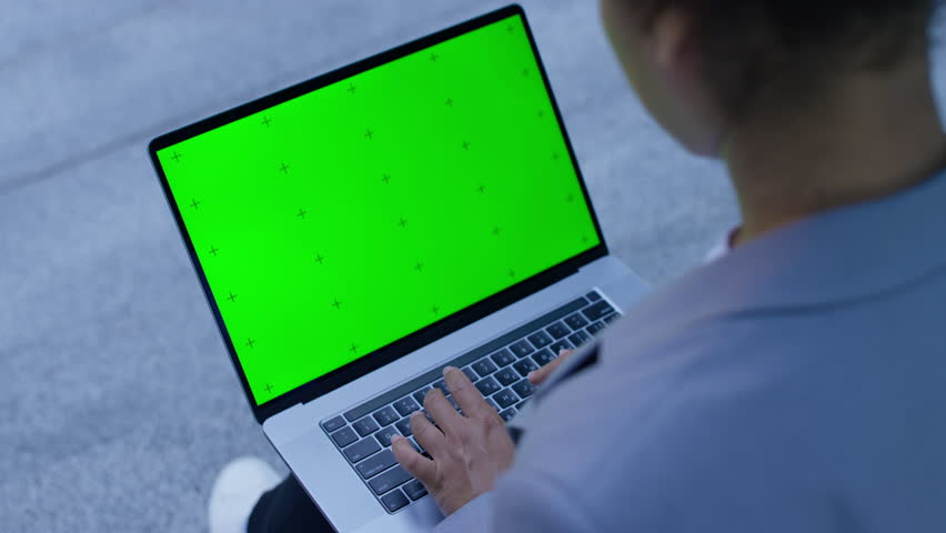 Close-up of hands typing on a laptop with a green screen outdoors, perfect for mockups, business, or technology-related concepts.