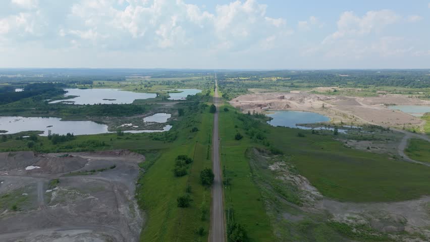 Long straight train track by gravel pit and lakes in Canada, forward drone