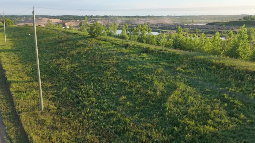 Power lines next to gravel pit and lakes in sunny Canada, rising drone
