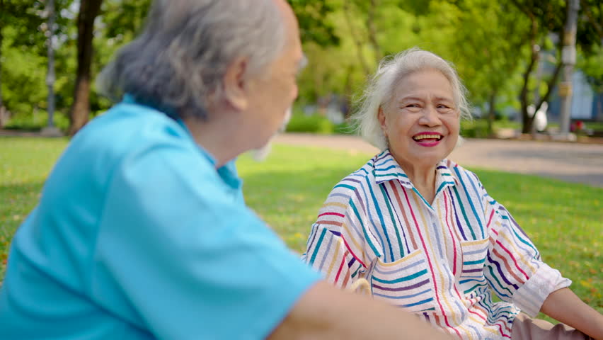 Senior asian man and woman couple of best friend enjoy a delightful picnic under the trees, sipping orange juice and sharing laughter in a park, creating lasting memories together, talk and relax 
