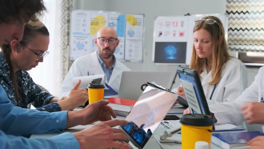 Doctors and interns in lab coats use laptops and tablets debating medical research at hospital seminar. Healthcare professionals discuss neuroscience, brain treatment and pharmaceutical innovations. - Powered by Shutterstock - Get 15% off with code: PIKWIZARD15
