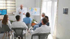 Bald doctor in white coat holding badge introduces himself during hospital seminar. Lecturer greets medical staff and residents, starting professional training and healthcare education. - Powered by Shutterstock - Get 15% off with code: PIKWIZARD15