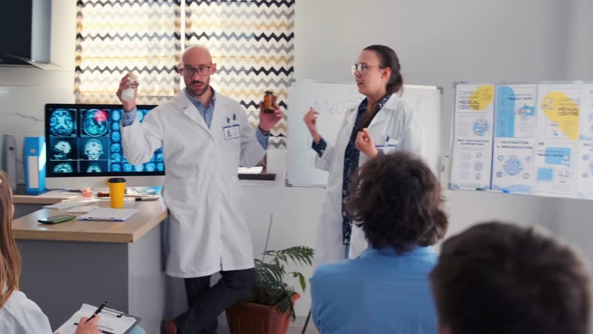 In a medical seminar, a pharmaceutical company representative promotes a new drug, but a female doctor takes the bottle and drops it to the floor, showing disapproval in front of colleagues.