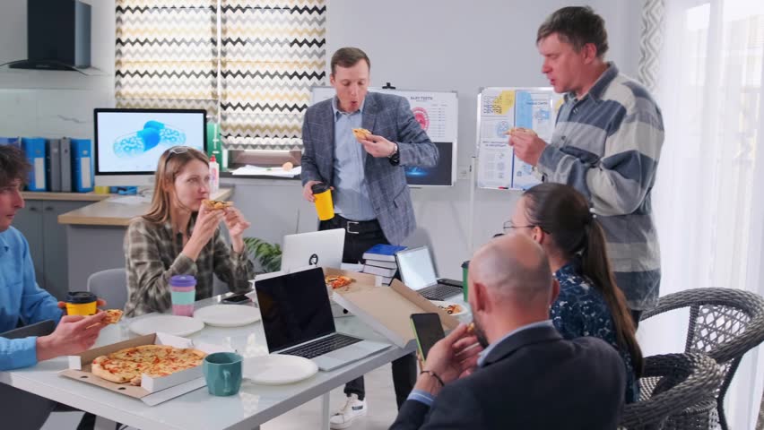 Group of colleagues in casual and business clothes taking a lunch break at the office table, eating pizza and drinking coffee. Informal teamwork atmosphere, laptops and documents visible. - Powered by Shutterstock - Get 15% off with code: PIKWIZARD15