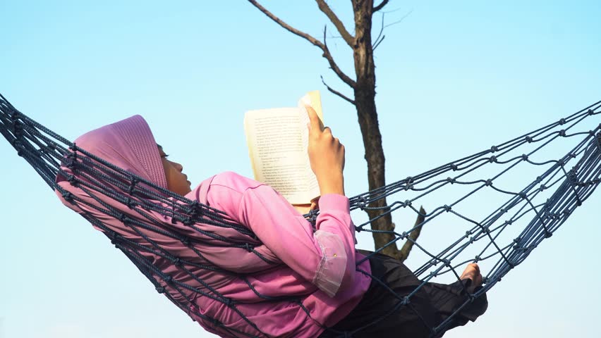 Girl wearing hijab reading a book while relaxing in a hammock - Powered by Shutterstock - Get 15% off with code: PIKWIZARD15