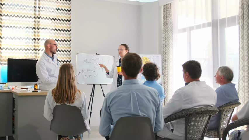 Bald pharmaceutical representative and chief doctor in white coat discuss new drug at hospital seminar. Active debate about product features and healthcare innovations with medical staff attending
