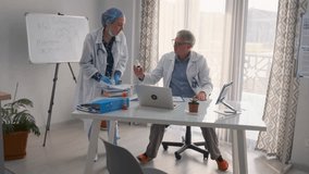 Senior male doctor and female physician in lab coats discussing a medicine bottle in modern office. They review medical notes, use laptop and tablet, and stand near a whiteboard with chemical formula. - Powered by Shutterstock - Get 15% off with code: PIKWIZARD15