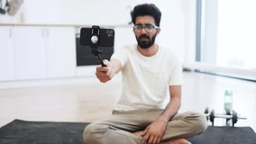 Young adult male explaining fitness and health routines on camera while seated on yoga mat indoors. - Powered by Shutterstock - Get 15% off with code: PIKWIZARD15