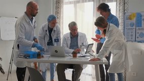 Group of doctors in lab coats actively debating medical research and scientific reports. Senior physician leads discussion on suitability of new drugs. Team studies data and clinical papers in office. - Powered by Shutterstock - Get 15% off with code: PIKWIZARD15