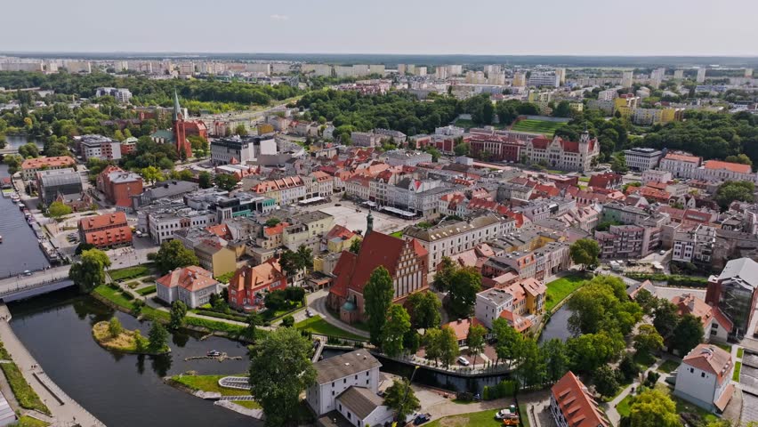 Aerial flyover of historic Bydgoszcz with church roof, trees, and city activity