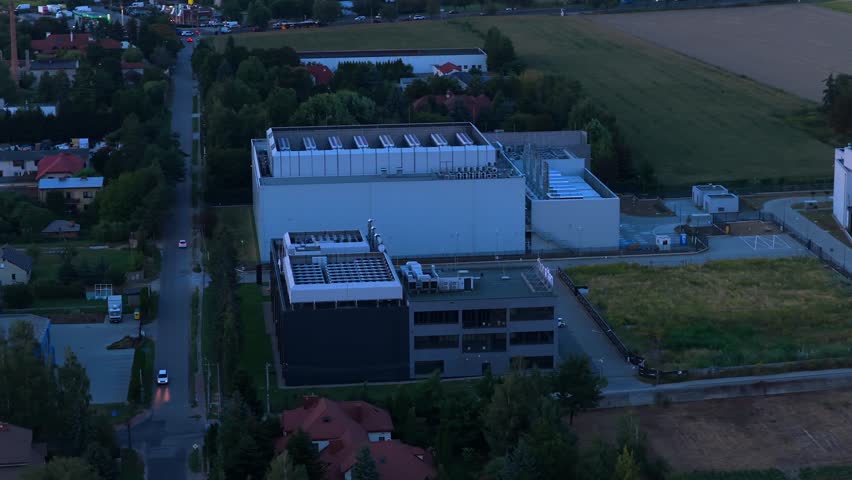 Modern data center facilities with modern IT infrastructure in rural suburbia or warsaw city. Night scene after sunset. Aerial view. Traffic on highway in distance. Orbit shot at dusk. Poland, Europe.