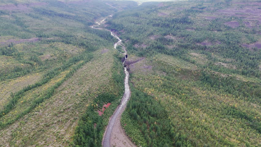 Aerial view along a winding river gorge cutting volcanic basalt in the Putorana Plateau near Lake Lama. Wild taiga, tiny rapids and a dark rock portal emphasize remote nature and adventure travel