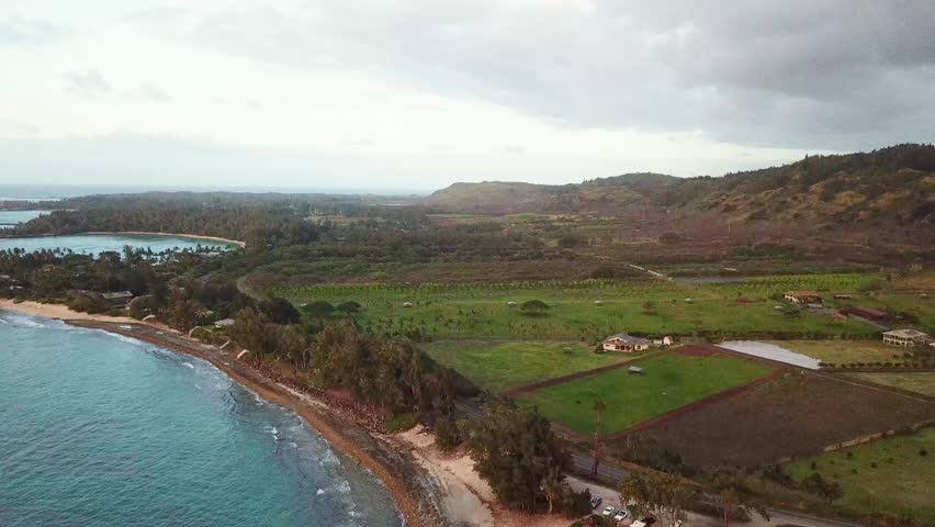 Cloudy day over Hawaii island. Aerial wide shot. Agricultural fields and sandy beach of Kawela. Panorama view with hills. Coastline with clear water of ocean.