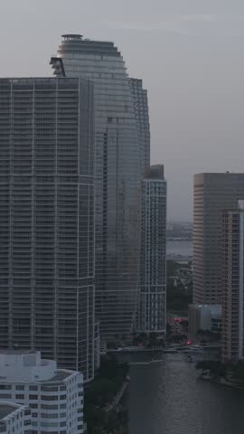 A vertical drone view of Brickell cityscape at dusk with tall buildings overlooking the Miami River in Miami, Florida, United States