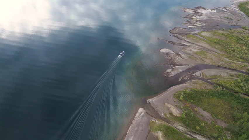 Aerial view of a speed boat tracing long wakes on Lake Lama beside a bright curved shoreline, Putorana Plateau, Russia. Soft morning light shows clear water and inspires adventure travel