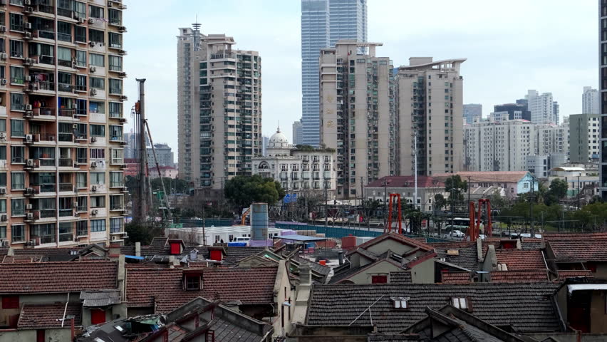 Stark contrast between traditional Shanghai neighborhood with old rooftops and a modern cityscape of towering residential and commercial buildings