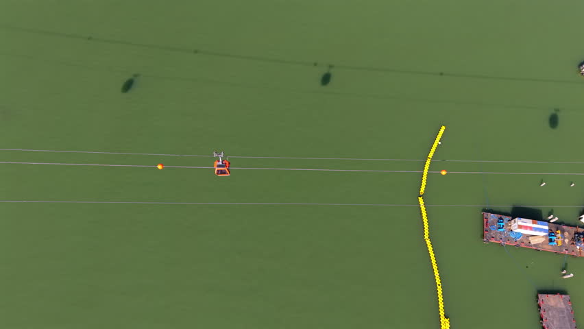 Cable car traversing Balneario Camboriu bay, gliding over yellow buoys near small pier under bright sunlight, top down Aerial view