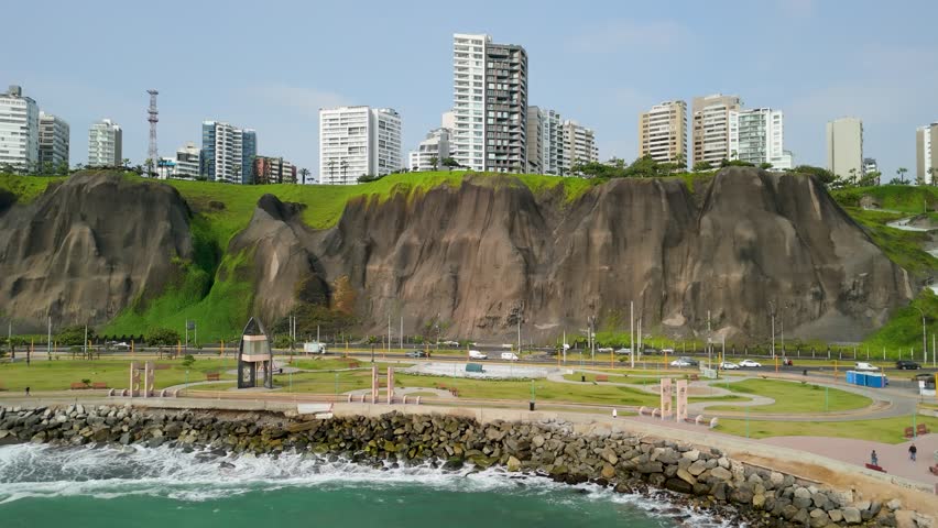 Dramatic cliffs of the Costa Verde, capturing the modern Miraflores cityscape above and the Pacific Ocean shoreline below - aerial trucking shot