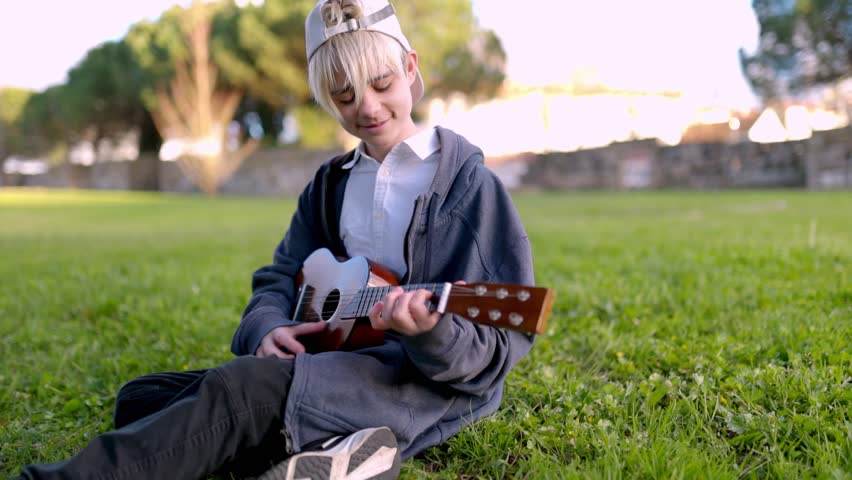 Young boy playing ukulele in park