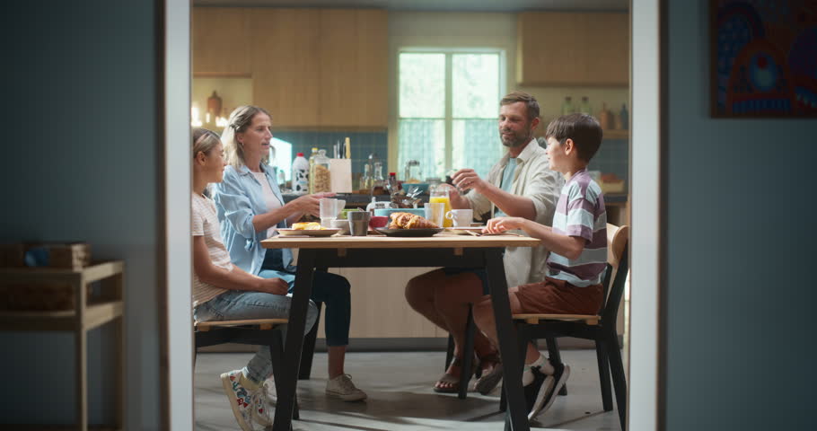 Family Gathers for a Joyful Breakfast Meal in a Kitchen, Passing Dishes, Smiling, and Talking. The Father Pours Orange Juice Friendly, and Filled With Laughter and Care.