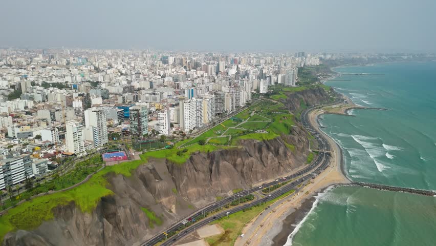 Vast cityscape of Lima, Peru, perched atop the dramatic green cliffs of the famous Costa Verde coastline - sweeping high-altitude aerial parallax shot