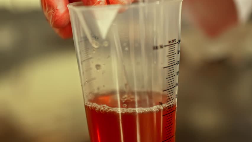 Scientist testing red liquid drops in a refractometer under precise lab conditions.