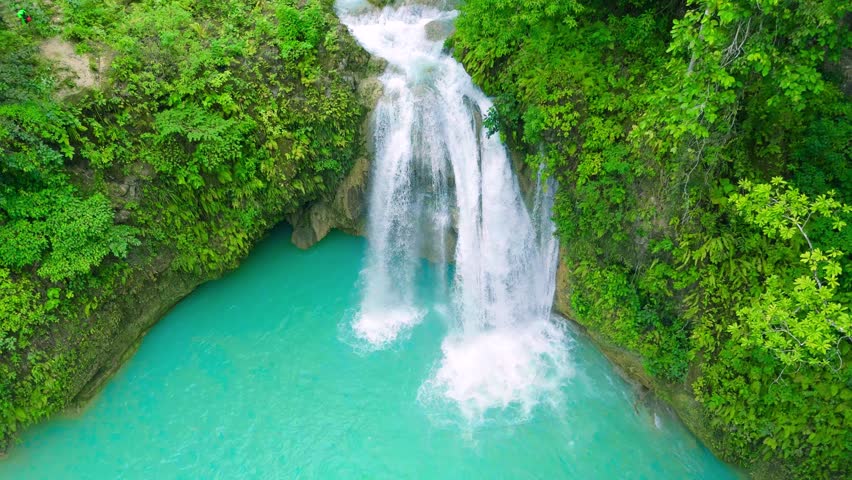 Aerial view of a cascading waterfall plunging into a turquoise natural pool, surrounded by green tropical foliage, Philippines.