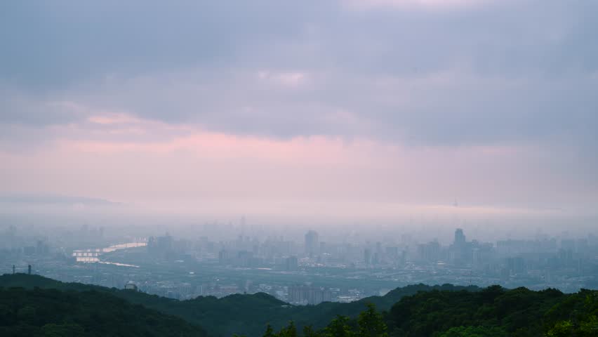 Aerial footage of Taipei City skyline shrouded in orange mist at dawn from Dadao Mountain in Shulin New Taipei City Taiwan with pink clouds and green hills foreground.