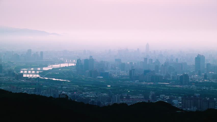 Dreamy dawn over Taipei City from Dadao Mountain, Taiwan. Orange, pink, and white clouds create a mystical haze over the urban landscape.