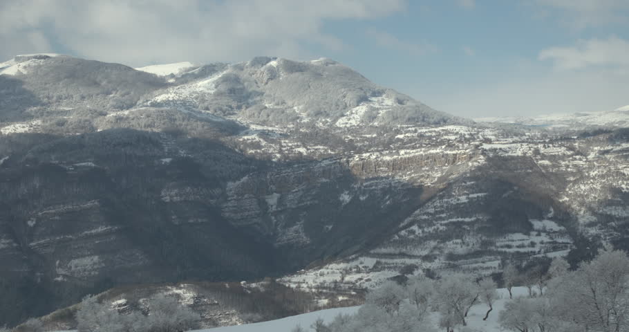Slow cinematic drone pan across majestic snow-covered mountain peaks, revealing pristine alpine wilderness, cold beauty, adventure, winter sports, exploration, and dramatic cinematic atmosphere.