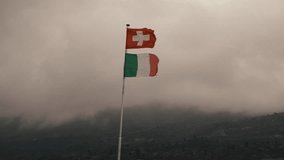 flag of Switzerland over flag of Italy. Italian-Swiss border in mountains. two flags fluttering in wind. on background mountains in clouds fog. white cross on red background. Tricolor green white red - Powered by Shutterstock - Get 15% off with code: PIKWIZARD15