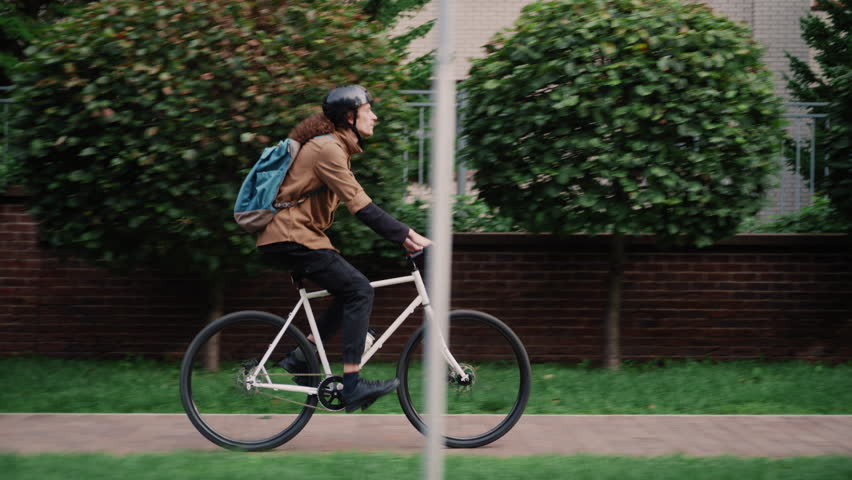 Smooth slider shot of a young man biking in a peaceful suburban area surrounded by greenery.