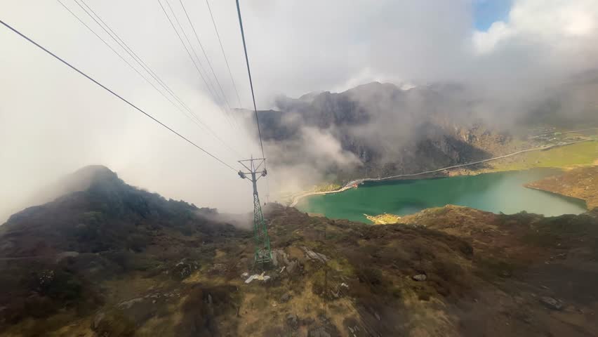 Ropeway at Tsomgo Lake (Changu Lake), Sikkim, India. Gondola glides above alpine landscape, passing through clouds on a sunny day with stunning Himalayan mountain views.