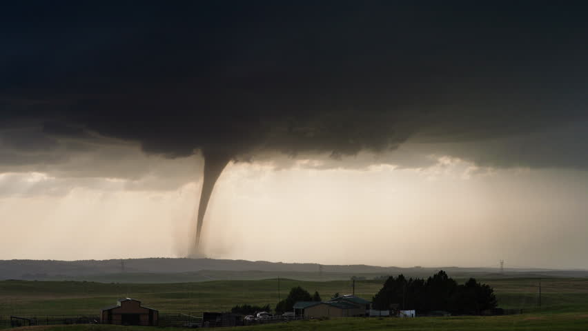 A rotating supercell produces a powerful tornado over a rural landscape, with dramatic cloud structure, strong rotation, and intense atmospheric energy on display